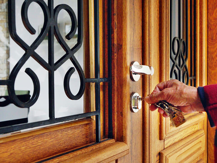 Close-up view of a man using keys to open a wood stained front door with black decorative metal over the windows