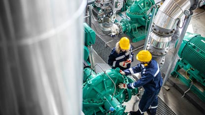 Gas and oil industrial workers working together and checking pipeline and engine pumps in factory.