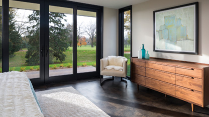 Bedroom with bed, carpet, wardrobe, and single chair in the view with large glass windows in the background overseeing green land