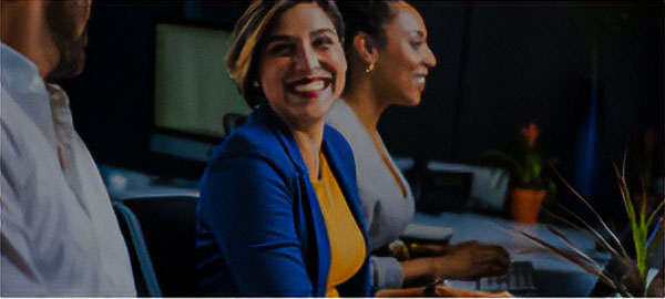 Woman in a yellow business shirt and blue jacket having a conversation with coworkers